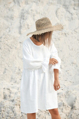 Stylish girl in trendy summer linen dress straw hat posing on the sand. Boho style