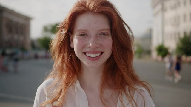 Face young sunshine woman with red hair look at camera smile stand in the city streets summer beautiful lady portrait happy outdoor close up slow motion