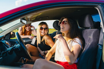 Two young attractive girls sit in car salon and chatting with third behind window, female positive travel adventures.