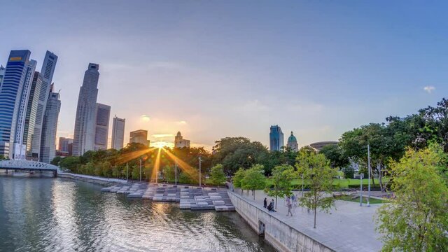 Sunset over Singapore skyscrapers skyline with white Anderson Bridge and a few towers of financial district near esplanade park timelapse. Some green foliage on both sides.