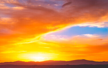 Sky with some clouds at sunset over the mountains, in orange and blue tones, in summer. 