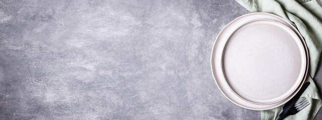 Banner with plates, black cutlery and linen napkin on stone table. Setting table with copy space in...