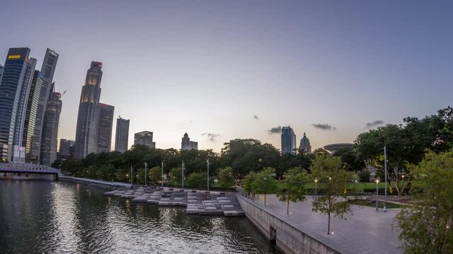 Singapore skyscrapers skyline with white Anderson Bridge and a few towers of financial district near esplanade park park day to night transition timelapse. Some green foliage on both sides.