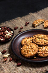 Homemade peanut cookies on a brown plate with raw peanuts in background