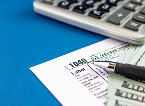 Tax form 1040, pen, calculator and dollars on a blue table. The concept of business taxation and business