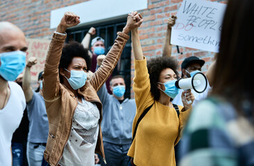 Two black women with face masks holding hands while participating in public demonstrations.