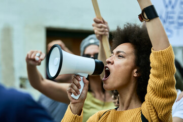 African American woman with raised fist shouting through megaphone on anti-racism protest. - obrazy, fototapety, plakaty