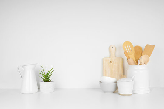 Kitchenware and utensils on a white shelf or countertop with a white wall background and copy space. Home kitchen cooking decor.