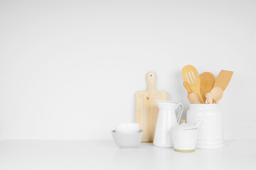 Fototapeta na wymiar Kitchenware and utensils on a white shelf or counter against a white wall background with copy space. Home kitchen cooking decor.