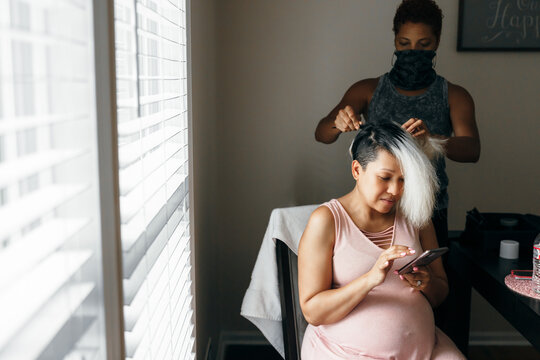 Pregnant black woman having hair done and self-care by hairdresser in mask during Covid-19