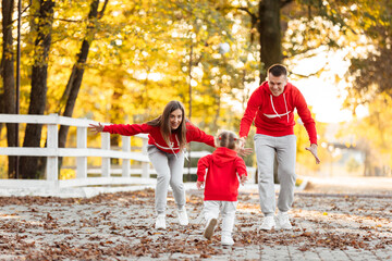 father, mother and little daughter are walking in the autumn park, happy family is having fun outdoors. father's, mother's and baby's day