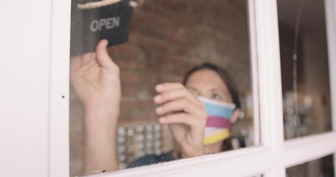 Female shop owner entrepreneur closing shop turning closed sign on window wearing face mask during Coronavirus Pandemic