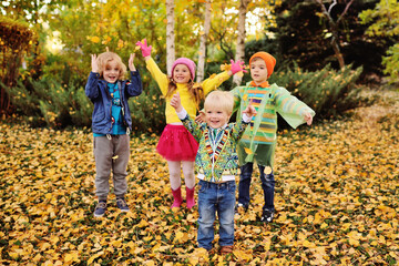 a group of preschoolers children play in the Park against the background of yellow autumn trees and throw up fallen leaves.