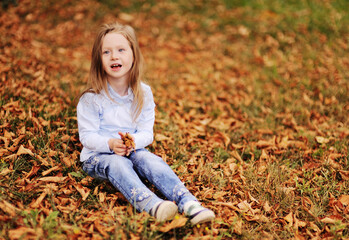 child - a little girl playing on the background of yellow fallen leaves and autumn Park.