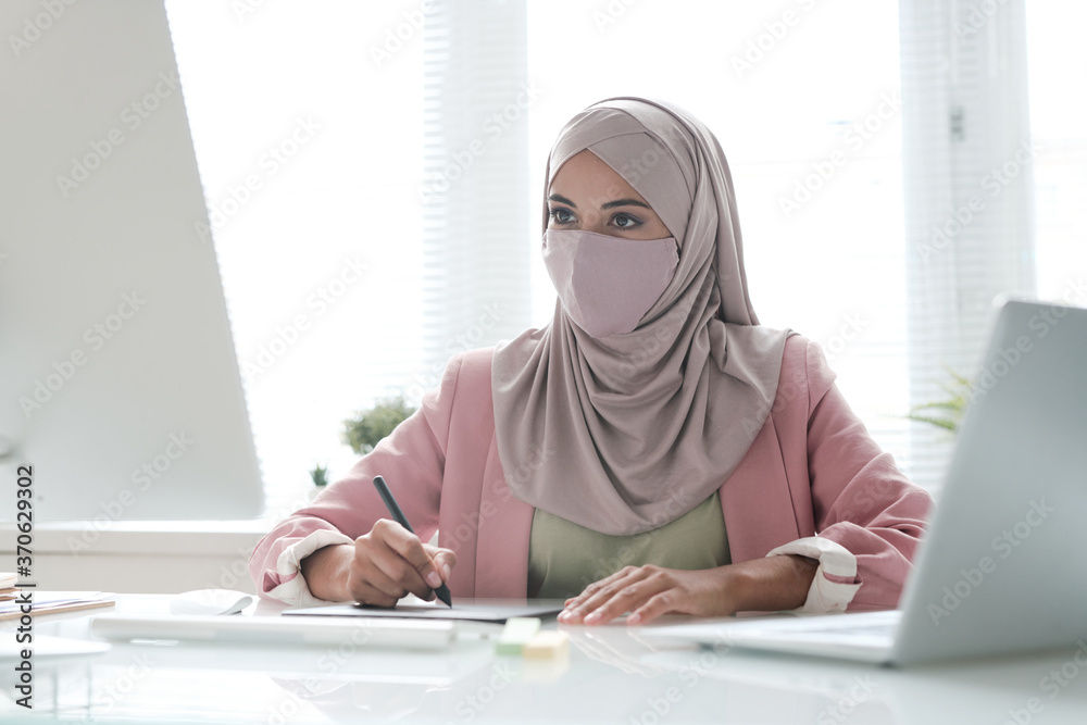 Poster young muslim businesswoman in hijab sitting at desk and using computer and digitizer while working o