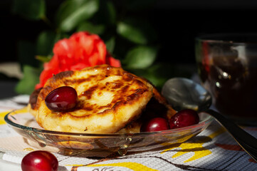 Pancakes, syrniki on a clear plate, doused with organic honey, are served with kizil. A traditional Ukrainian dish on a dark background with a blurred rose and a cup of hot coffee. Homemade food. 