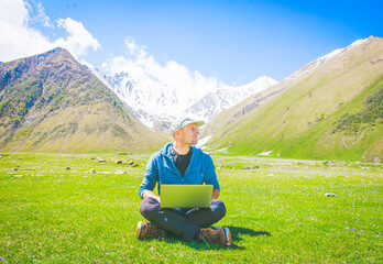 Bright positive image of male person sitting in casual clothes on the grass and looking to the right. Ideas and work online in post pandemic world.