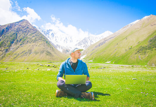 Bright positive image of male person sitting in casual clothes on the grass and looking to the right. Ideas and work online in post pandemic world.