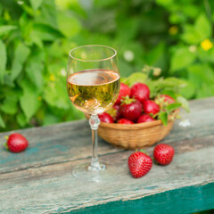Glass of rose wine served with fresh strawberries on wooden background. Picnic outdoor with pink wine and berries.