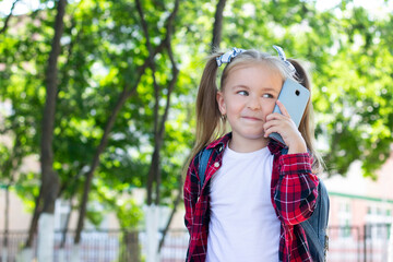 happy schoolgirl with a backpack talking on the phone on the street. in a white T-shirt and a plaid shirt