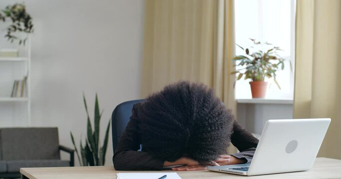 Overworked student girl worker sleeping at desk with laptop feels headache tired. Unproductive employee mixed race woman lying on table fall asleep feeling boredom, need rest break, insomnia concept