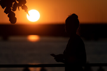 A silhouette of a happy young female walking on the shore admiring the sunset. 