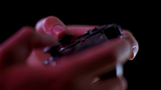 Playing video games in a darkened room with a black background close up on a small controller joystick playing quickly soft focus
