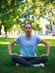 Naklejka na ściany i meble Concentrated young girl doing yoga exercises in summer green city park