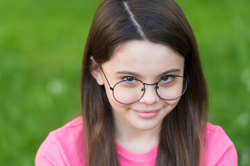 Little girl wear vintage rim eyeglasses green lawn background, shy baby concept