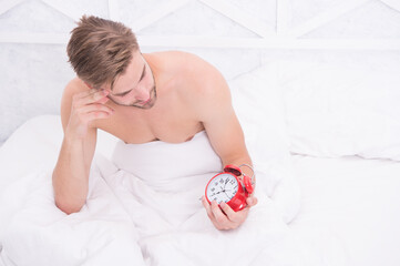 Morning time. Sleepy man look at alarm clock in bed. Sexy guy awake in morning. Good morning. Rise...