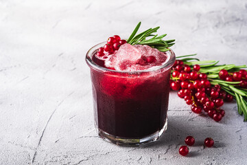 Fresh ice cold fruit cocktail in glass, refreshing summer red currant berry drink with rosemary leaf on stone concrete background, angle view