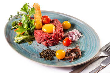 Traditional German food. Mett, Hackepeter on a plate with raw egg, tomatoes, parsley and chopped onions