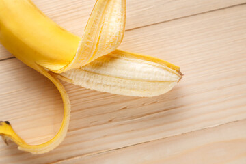Partially peeled ripe yellow banana on the wooden table in soft focus. Close up view.