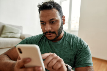 Checking. Close up of young man using smartphone app while having morning workout at home. Freshman...