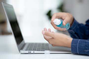 Hand of man work from home with alcohol gel or sanitizer for cleaning hand and protect coronavirus or covid-19, new normal, quarantine and social distancing, businessman using laptop computer.