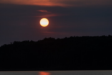Glowing red sun setting over the trees