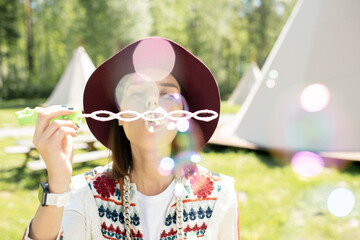 Carefree young woman in hat making bubble wand while having fun outdoors