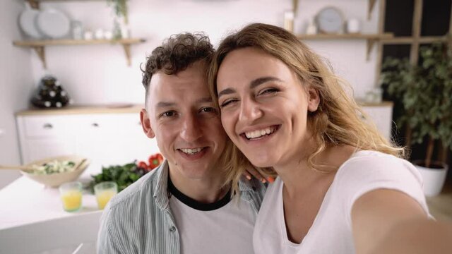 Close up of Lovely Young Couple Taking Selfie Video or Making Video Call, Talking to Camera, Laughing, Kissing, Showing Love while Sitting in the Kitchen and Having Breakfast.