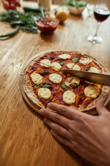 Slices. Close up shot of man cutting hot freshly baked pizza on the table. Hobby, lifestyle