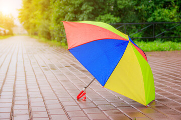 An open colored umbrella stands on the asphalt. Summer rain. Article about choosing an umbrella. Children's bright umbrella. . Copy space