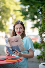 Fototapeta premium Charming brown-haired female reading sitting in cafe, reading newspaper