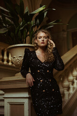 Luxury curly blonde woman wearing trendy sequin mini dress with big shoulders  posing in beautiful old building. Film grain effect