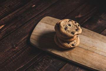 Fresh baked chocolate chip cookies single stacked on a wooden board. 