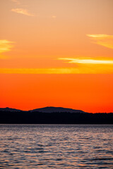 Hills are silhouetted against a burning orange sunset sky