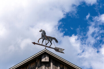 A vintage trotting horse whirligig weathervane twirls on the rooftop of an old barn. - obrazy, fototapety, plakaty