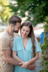 Obraz premium Bearded male hugging female in blue dress, pressing his nose to her head
