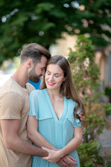 Bearded male hugging tenderly female in blue dress, pressing his forehead to her face