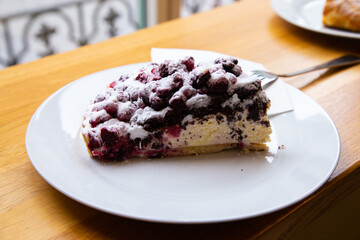 A piece of delicious cherry cake or tart with cream and caster sugar in the white plate on wooden table