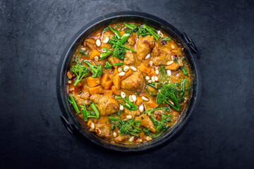 Modern style African crocodile cheeks curry with sweet potato, broccoli and peanuts as top view in a modern design cast iron pot - obrazy, fototapety, plakaty