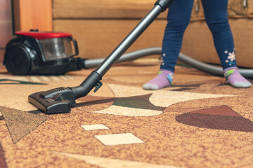 A small child vacuums a carpet with a vacuum cleaner